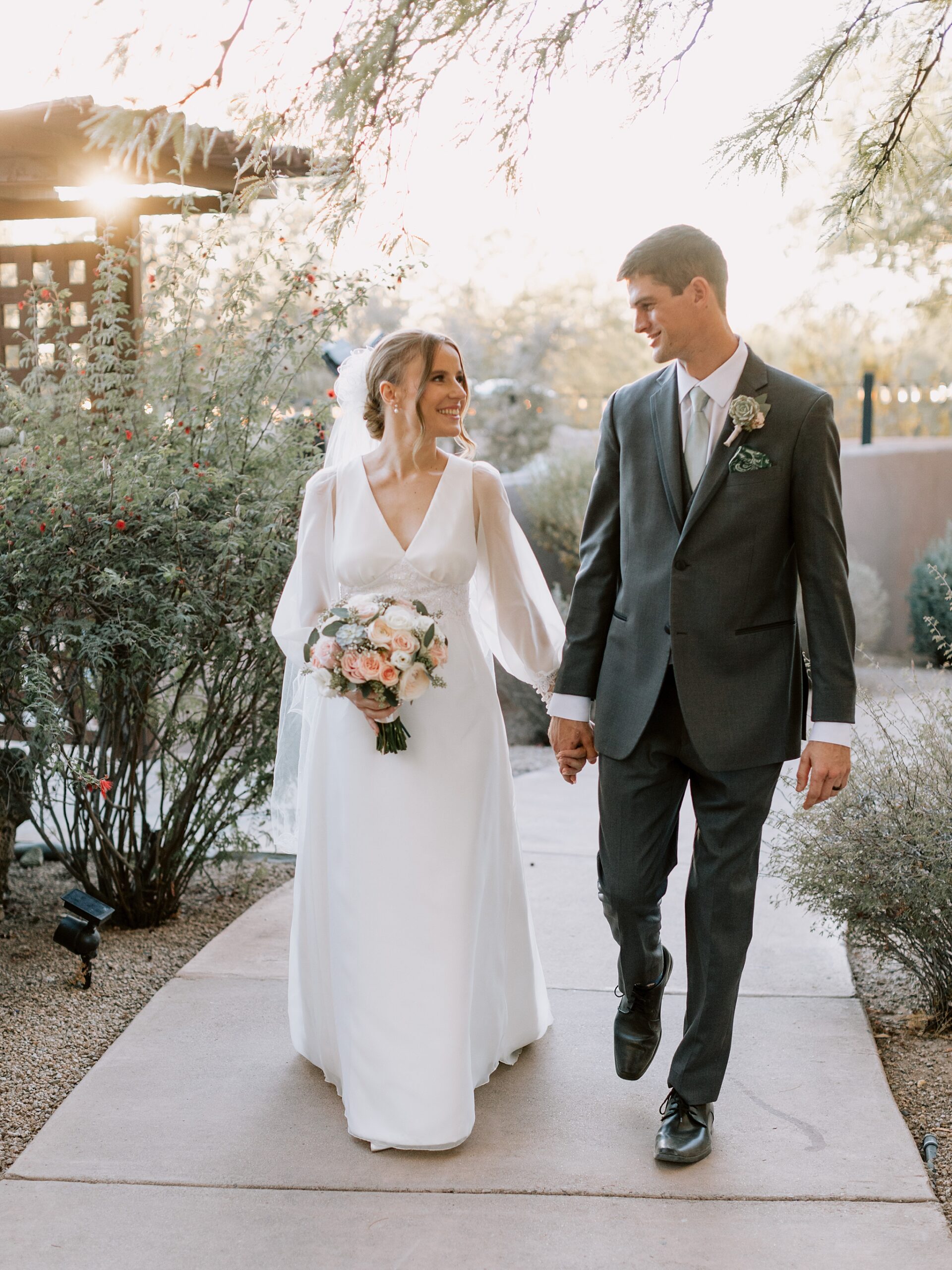 Bride and groom strolling through the desert landscape at The Boulders Resort, with warm golden light surrounding them