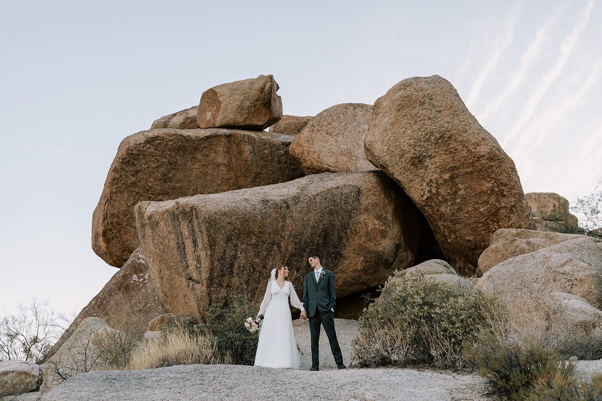 Bride and groom strolling through the desert landscape at The Boulders Resort, with warm golden light surrounding them