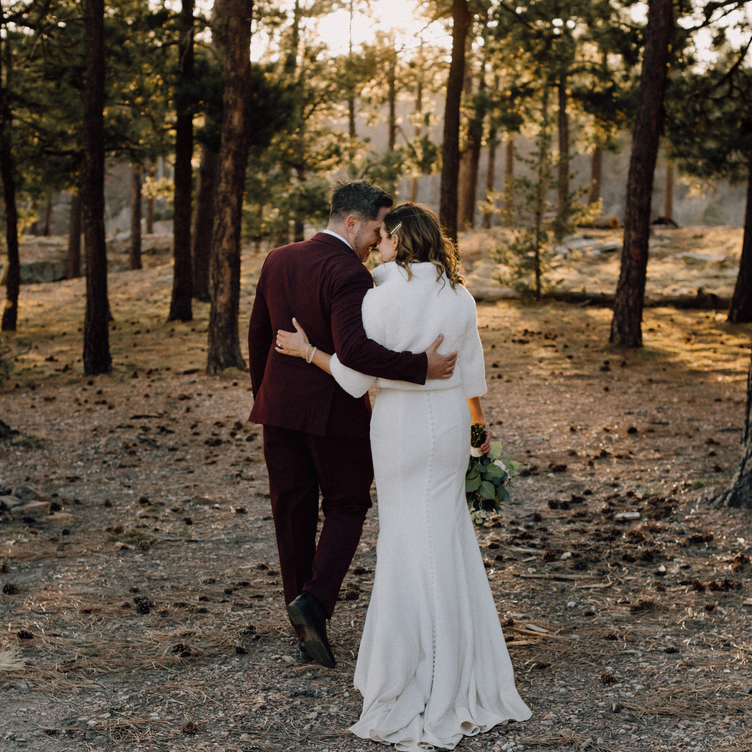 Candid wedding photo of a couple walking quietly in the woods as the sun sets in the background