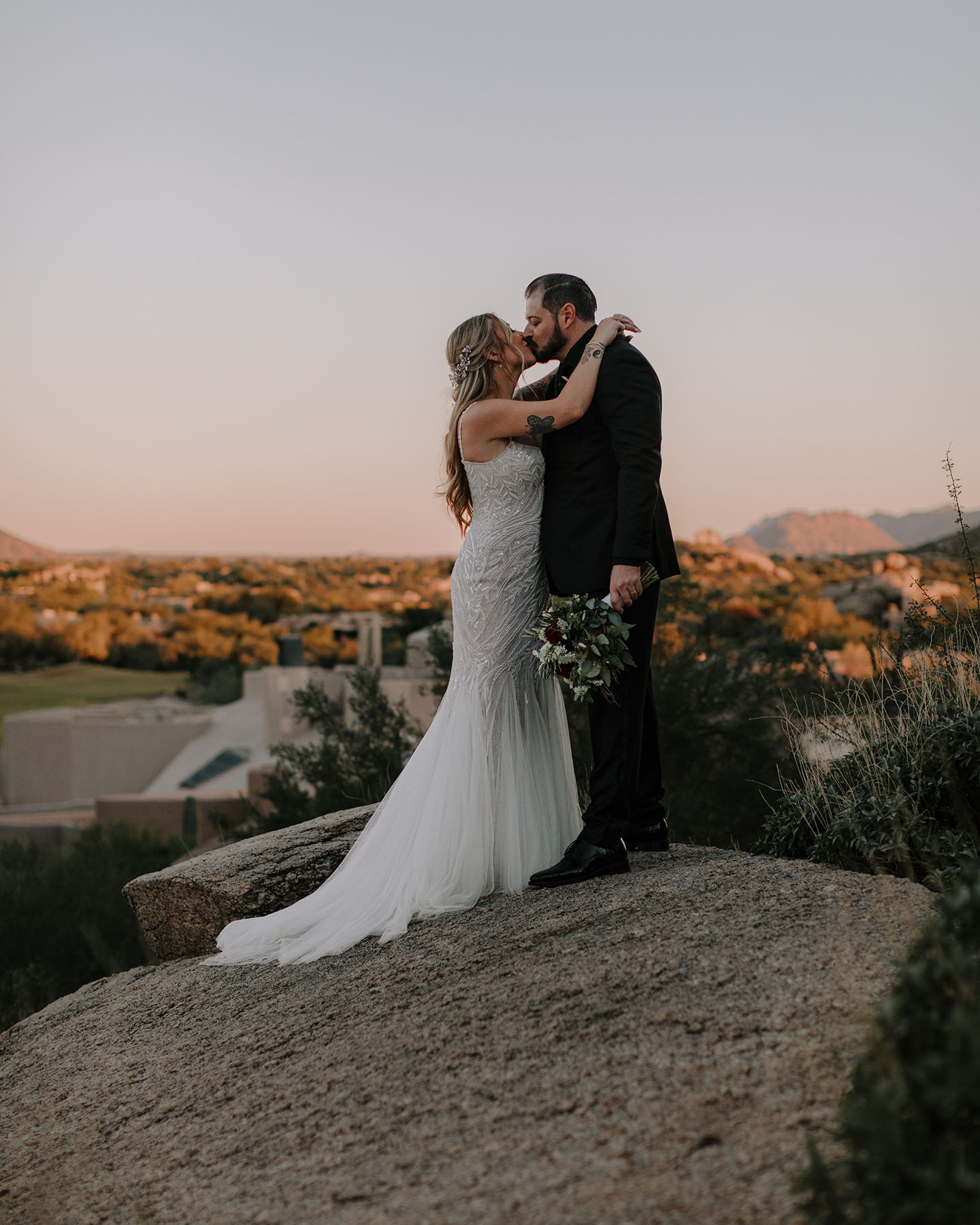 Bride and groom kissing on a boulder overlooking the desert at sunset at Promise Rock, Scottsdale Arizona.