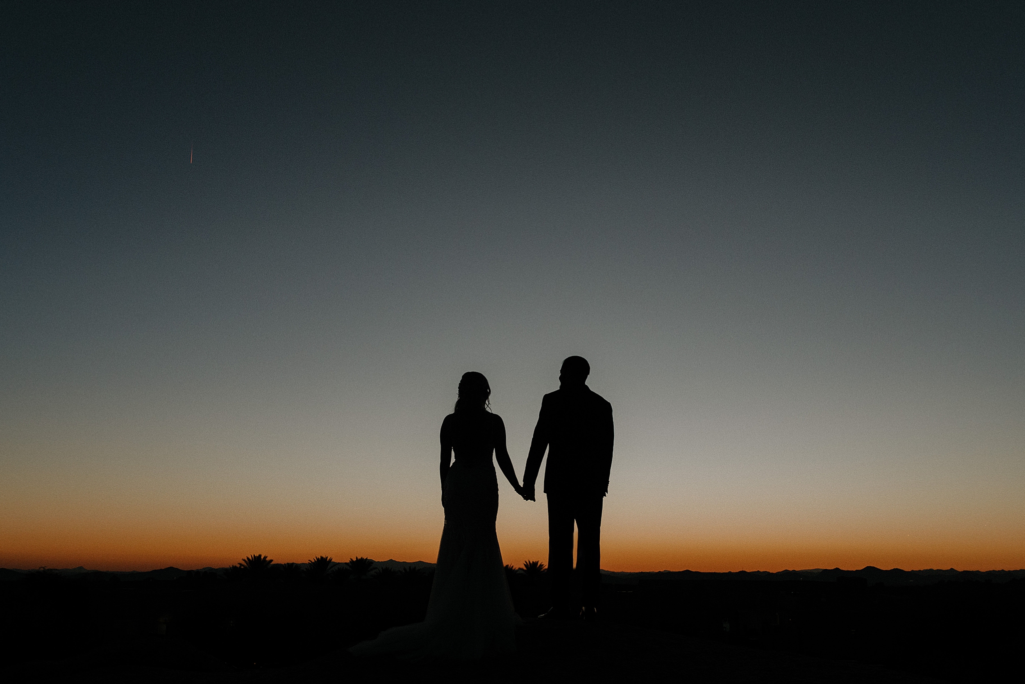 Bride and groom silhouetted against the desert sky as the sun sets behind the rocks