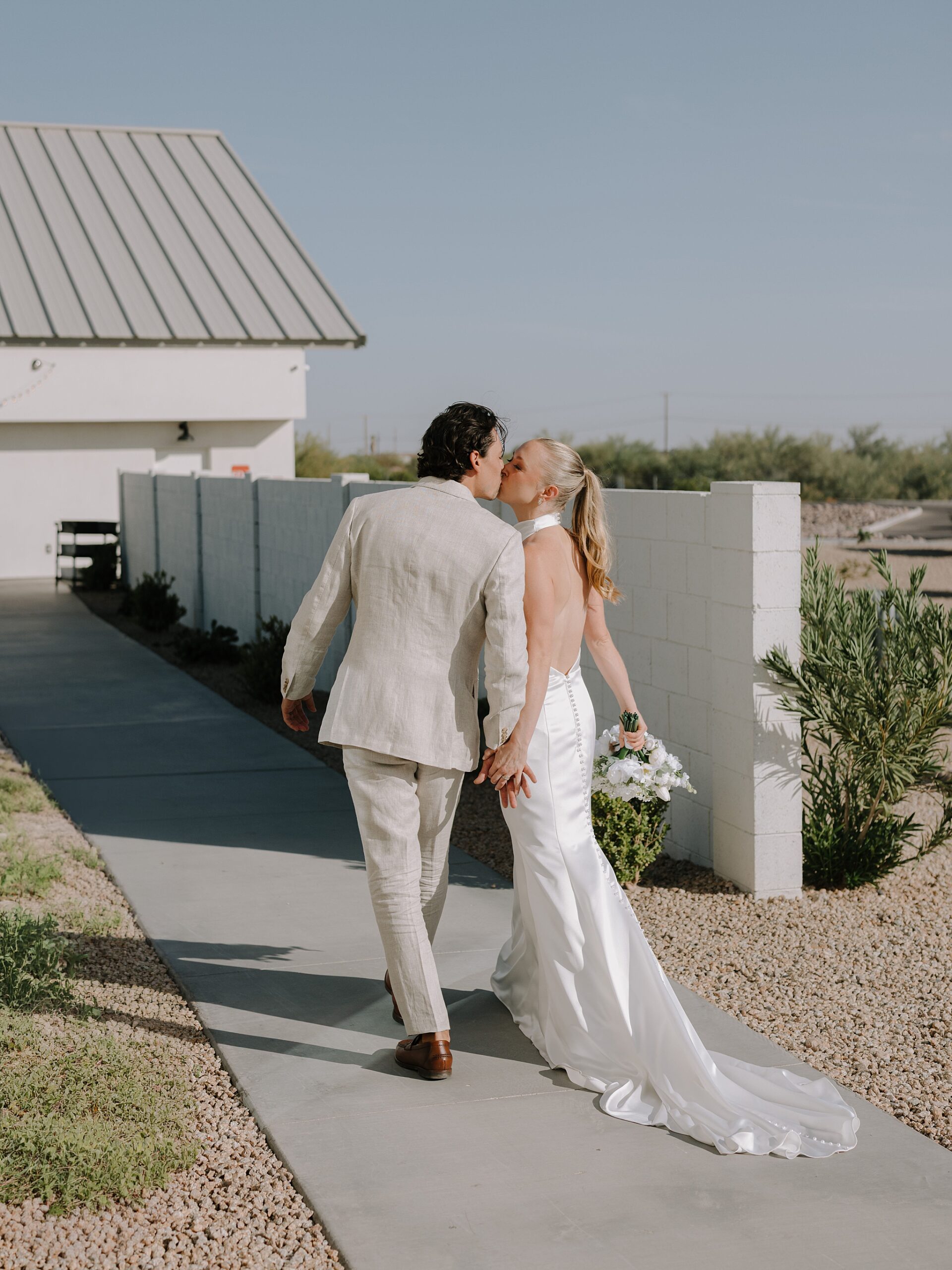 Bride in an open-back wedding dress walking with the Groom at Desert View Weddings & Events in bright Arizona light
