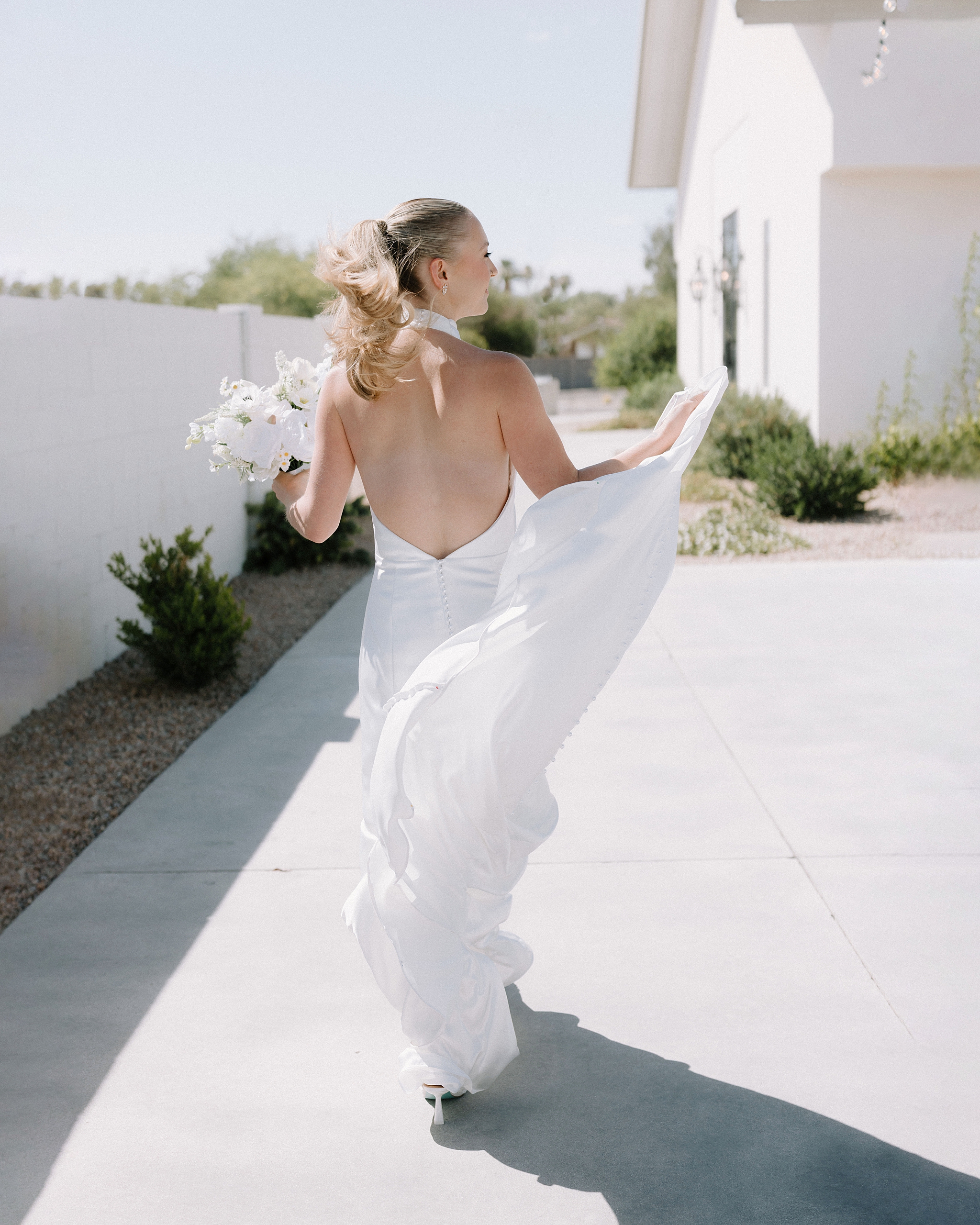 Bride in an open-back wedding dress walking at Desert View Weddings & Events in bright Arizona light